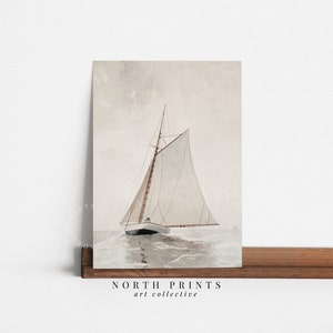 Puede incluir: Una pintura de acuarela de un velero con una vela blanca y un m&aacute;stil marr&oacute;n, navegando en un mar tranquilo de color gris claro. El cielo es de un rosa suave y p&aacute;lido. La pintura est&aacute; enmarcada y tiene el texto "NORTH PRINTS art collective" en la parte inferior.