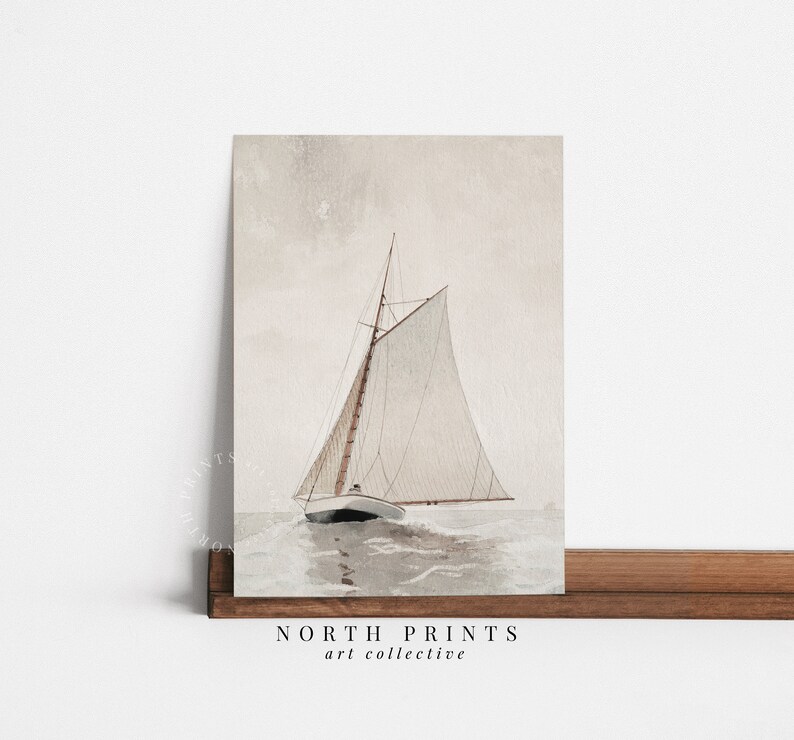 Puede incluir: Una pintura de acuarela de un velero con una vela blanca y un m&aacute;stil marr&oacute;n, navegando en un mar tranquilo de color gris claro. El cielo es de un rosa suave y p&aacute;lido. La pintura est&aacute; enmarcada y tiene el texto "NORTH PRINTS art collective" en la parte inferior.