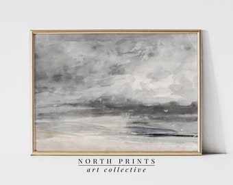 Puede incluir: Una pintura de acuarela enmarcada de un paisaje marítimo con un cielo tormentoso y una costa distante. La pintura está en tonos de gris y blanco, con toques de rosa y azul. El marco es de madera clara y simple.