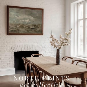 May include: A light wood dining table with six chairs, a vase of white flowers, and a framed painting of a seascape hanging on a white brick wall. The text "NORTH PRINTS art collective" is visible on the table.