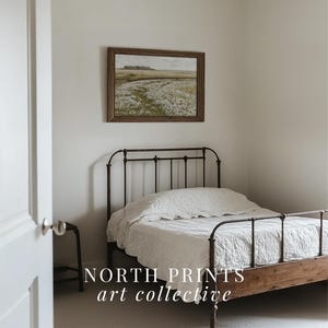 May include: A white bed with a black metal frame and a wooden headboard. The bed is in a room with white walls and a framed landscape painting above the headboard. The text "NORTH PRINTS art collective" is visible in the bottom of the image.