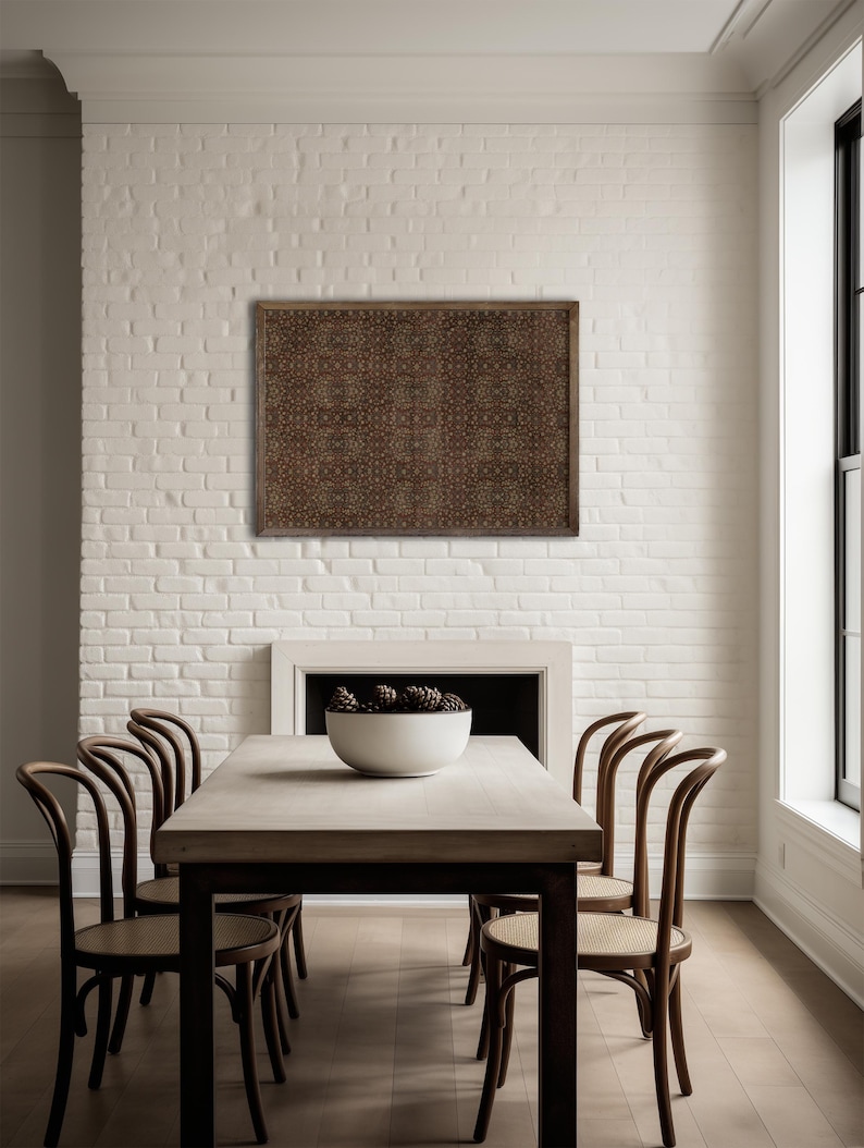 May include: A dining room with a wooden table and six chairs. A patterned artwork hangs on the white brick wall above a fireplace. A white bowl with pinecones sits on the table. The room has a minimalist design.