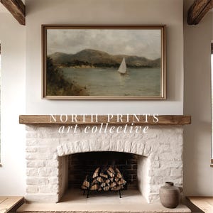 May include: A framed landscape painting of a sailboat on a lake, mounted above a white brick fireplace. The painting has a light brown frame and depicts a cloudy sky and green hills. The text "NORTH PRINTS art collective" is below the painting.
