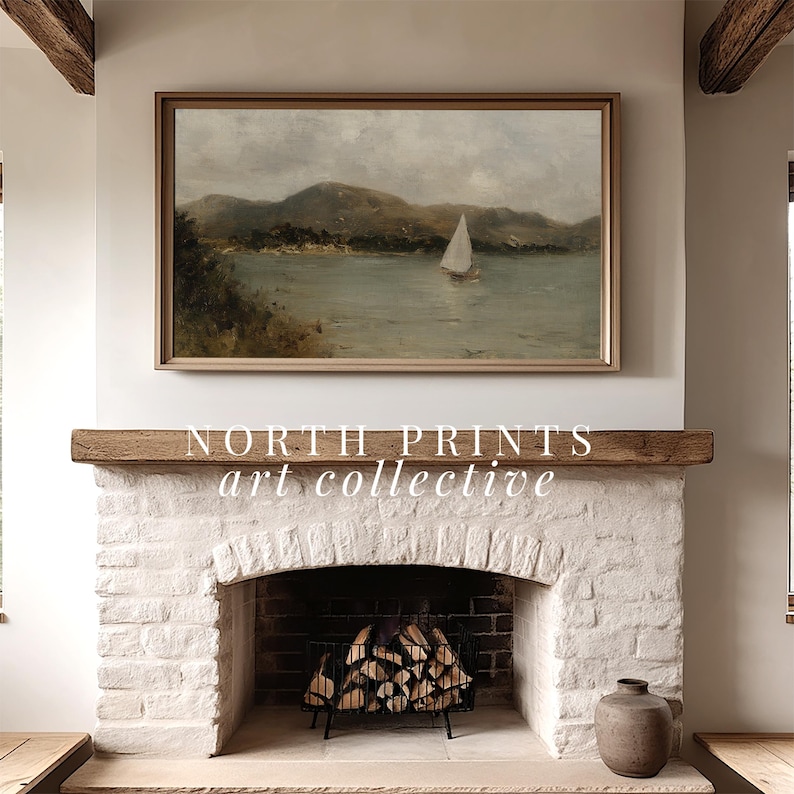May include: A framed landscape painting of a sailboat on a lake, mounted above a white brick fireplace. The painting has a light brown frame and depicts a cloudy sky and green hills. The text "NORTH PRINTS art collective" is below the painting.