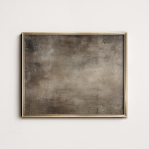 May include: A framed abstract painting with a gold-colored frame. The artwork features a muted color palette of browns and grays, with visible brushstrokes and texture. The painting is rectangular and mounted on a white wall.