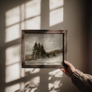 Puede incluir: Una pintura de paisaje rectangular en un marco de madera marr&oacute;n oscuro. La obra representa una escena de bosque nevado con &aacute;rboles de hoja perenne bajo un cielo nublado y apagado. La pintura presenta tonos grises, blancos y verdes apagados.