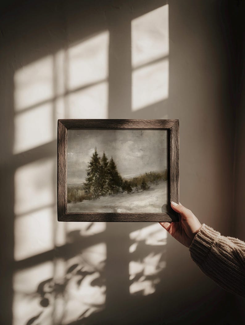 Puede incluir: Una pintura de paisaje rectangular en un marco de madera marr&oacute;n oscuro. La obra representa una escena de bosque nevado con &aacute;rboles de hoja perenne bajo un cielo nublado y apagado. La pintura presenta tonos grises, blancos y verdes apagados.
