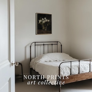 May include: A white metal bed frame with a white linen headboard and a white linen comforter. The bed is in a bedroom with white walls and a framed floral print hanging above the headboard. The text "NORTH PRINTS art collective" is visible in the bottom of the image.