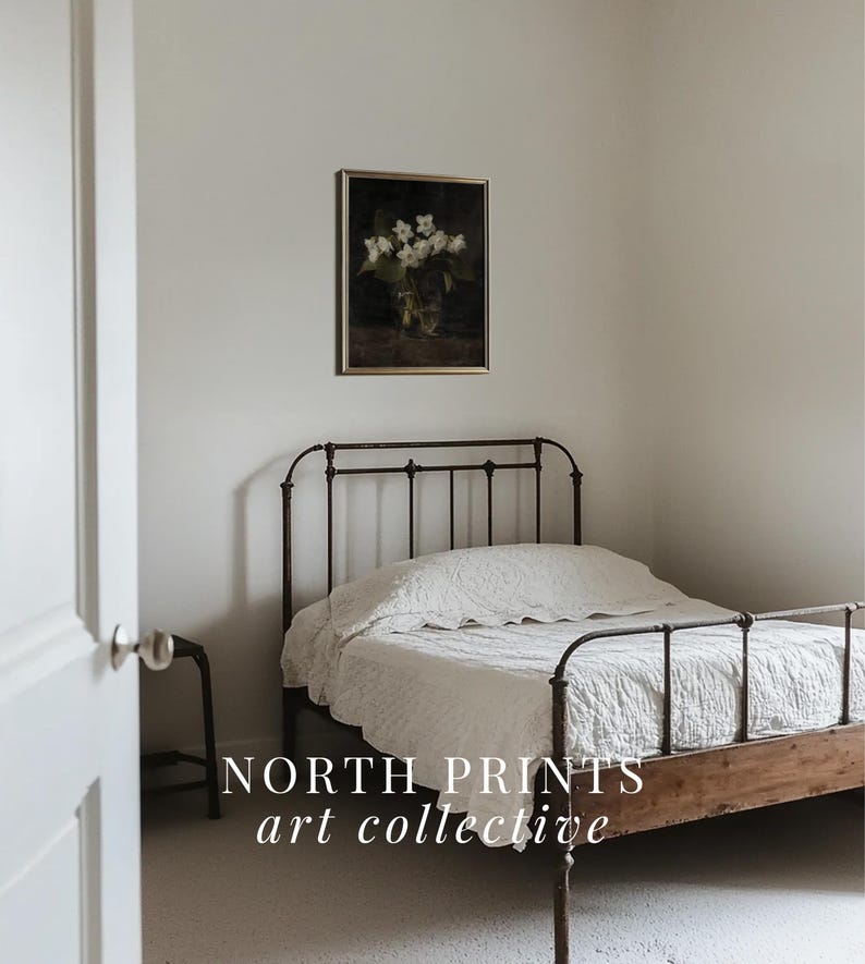 May include: A white metal bed frame with a white linen headboard and a white linen comforter. The bed is in a bedroom with white walls and a framed floral print hanging above the headboard. The text "NORTH PRINTS art collective" is visible in the bottom of the image.