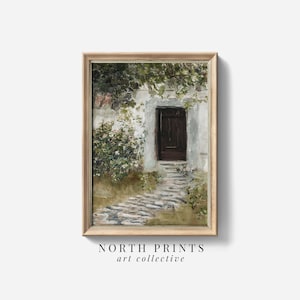 以下が含まれることがあります： 石畳の小道が暗い木のドアへと続く、額装されたヴィンテージアートプリント。ドアは白いスタッコの壁にあり、つる植物と花が咲いています。「NORTH PRINTS art collective」と表示されています。