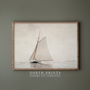 May include: A vintage watercolor painting of a sailboat with white sails on a calm sea. The painting is framed in a natural wood frame. The text "NORTH PRINTS vintage art collective" is printed below the image.