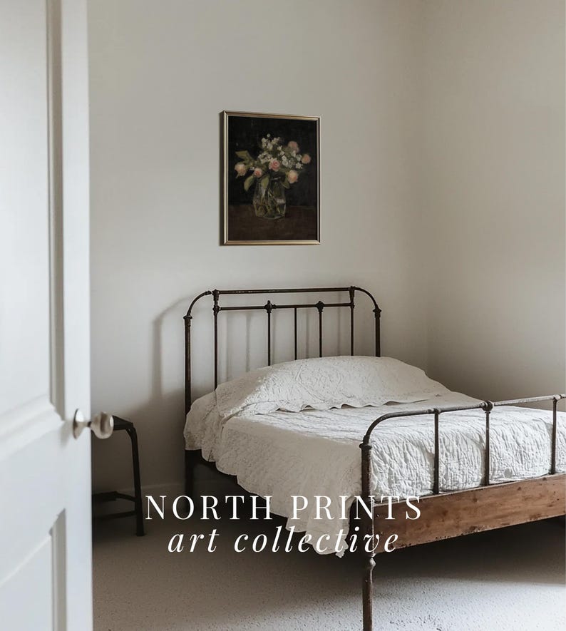 May include: A white bed with a black metal frame and a white bedspread. A framed painting of a bouquet of flowers in a vase is hanging on the wall behind the bed. The text "NORTH PRINTS art collective" is printed on the floor in front of the bed.