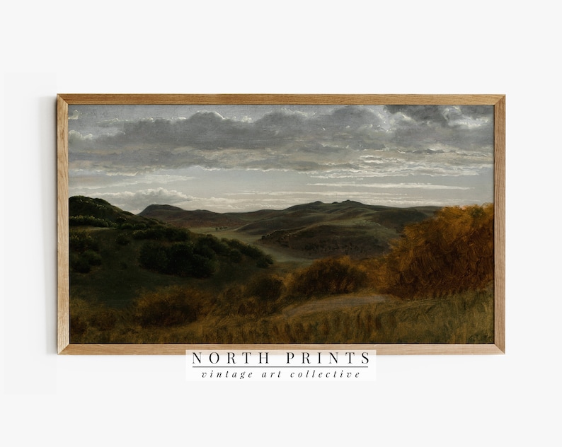 K&ouml;nnte beinhalten: Ein Vintage-Landschaftsgem&auml;lde, das einen sanften, gr&uuml;nen H&uuml;gel mit einem bew&ouml;lkten Himmel zeigt. Das Gem&auml;lde ist in einem hellbraunen Holzrahmen gerahmt. Der Text "NORTH PRINTS vintage art collective" ist unter dem Rahmen gedruckt.