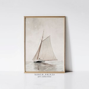 Puede incluir: Una pintura de acuarela enmarcada de un velero con velas blancas sobre un fondo azul claro y gris. El velero navega en una masa de agua con olas. La pintura est&aacute; enmarcada en un marco dorado. El texto "NORTH PRINTS art collective" est&aacute; impreso debajo de la imagen.