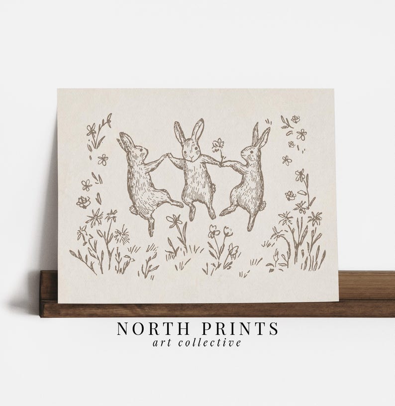May include: A black and white line drawing of three rabbits dancing in a field of flowers. The rabbits are holding hands and appear to be having fun. The drawing is on a light brown background.