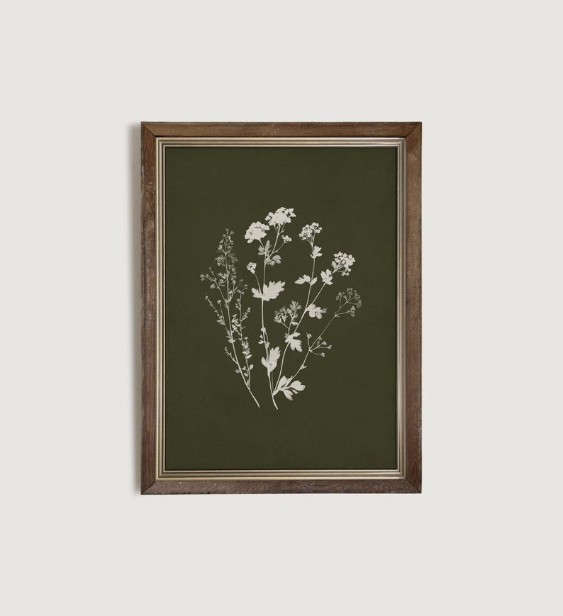 May include: A framed botanical print featuring white floral illustrations on a dark green background. The artwork is encased in a brown wooden frame, creating a vintage aesthetic. The print showcases detailed depictions of various plant species.