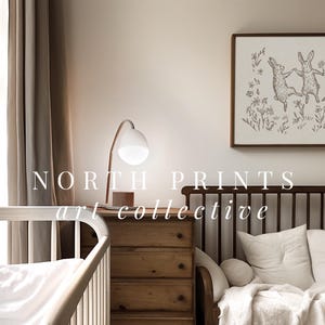 May include: A nursery room with a white crib, a wooden dresser, and a brown couch with white pillows. A framed print of three dancing rabbits hangs on the wall above the couch. The text "NORTH PRINTS art collective" is printed on the wall.