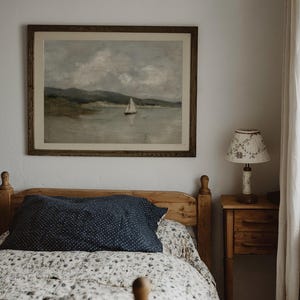 K&ouml;nnte beinhalten: Ein Schlafzimmer mit einem Holzbett, einem marineblauen Kissen mit wei&szlig;en Punkten und einer floral gemusterten Steppdecke. Ein gerahmtes Landschaftsbild eines Segelboots h&auml;ngt &uuml;ber dem Bett. Ein kleiner Nachttisch aus Holz mit einer Lampe befindet sich rechts.