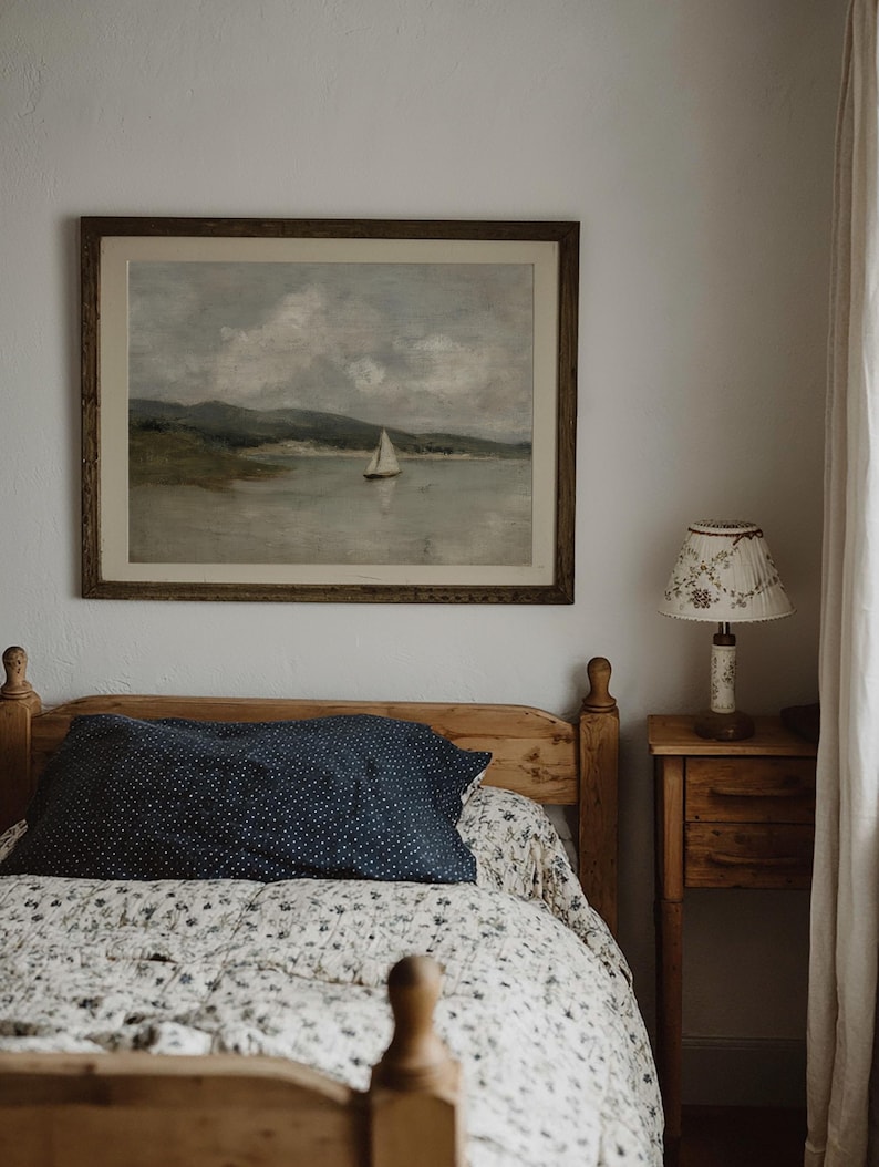 K&ouml;nnte beinhalten: Ein Schlafzimmer mit einem Holzbett, einem marineblauen Kissen mit wei&szlig;en Punkten und einer floral gemusterten Steppdecke. Ein gerahmtes Landschaftsbild eines Segelboots h&auml;ngt &uuml;ber dem Bett. Ein kleiner Nachttisch aus Holz mit einer Lampe befindet sich rechts.