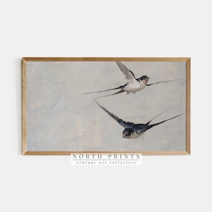 Puede incluir: Una pintura vintage enmarcada de dos golondrinas en vuelo contra un cielo azul claro. La pintura est&aacute; en un marco de madera con un acabado marr&oacute;n claro. El texto "NORTH PRINTS vintage art collective" est&aacute; impreso debajo del marco.