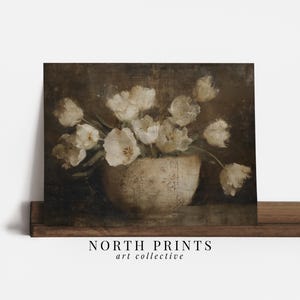 May include: A vintage-style print featuring a still life of white tulips in a cream-colored vase. The artwork has a dark, moody background and the text "NORTH PRINTS art collective" at the bottom.