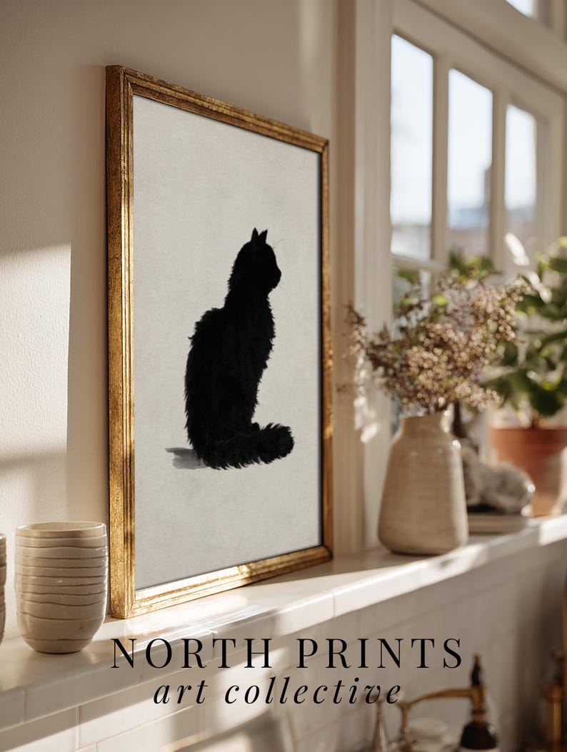 Peut inclure: Impression d'art encadr&eacute;e repr&eacute;sentant une silhouette de chat noir sur fond neutre, dans un cadre dor&eacute;. L'&oelig;uvre fait partie de la collection "art collective". L'impression est expos&eacute;e sur une &eacute;tag&egrave;re blanche pr&egrave;s d'une fen&ecirc;tre.