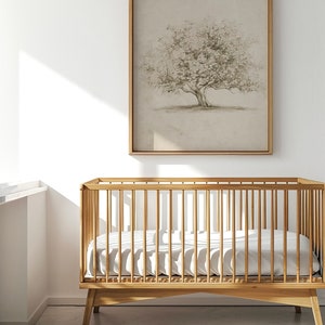 Op de afbeelding: Een houten wieg met een wit matras en een ingelijst tekening van een boom erboven. De tekst "NORTH PRINTS art collective" is onder de wieg gedrukt.