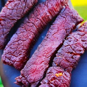 K&ouml;nnte beinhalten: Nahaufnahme von mehreren St&uuml;cken dunkelrotem Rindfleisch-Trockenfleisch. Das Trockenfleisch ist zu einem Stapel angeordnet und zeigt die Textur und Farbe des Fleisches.