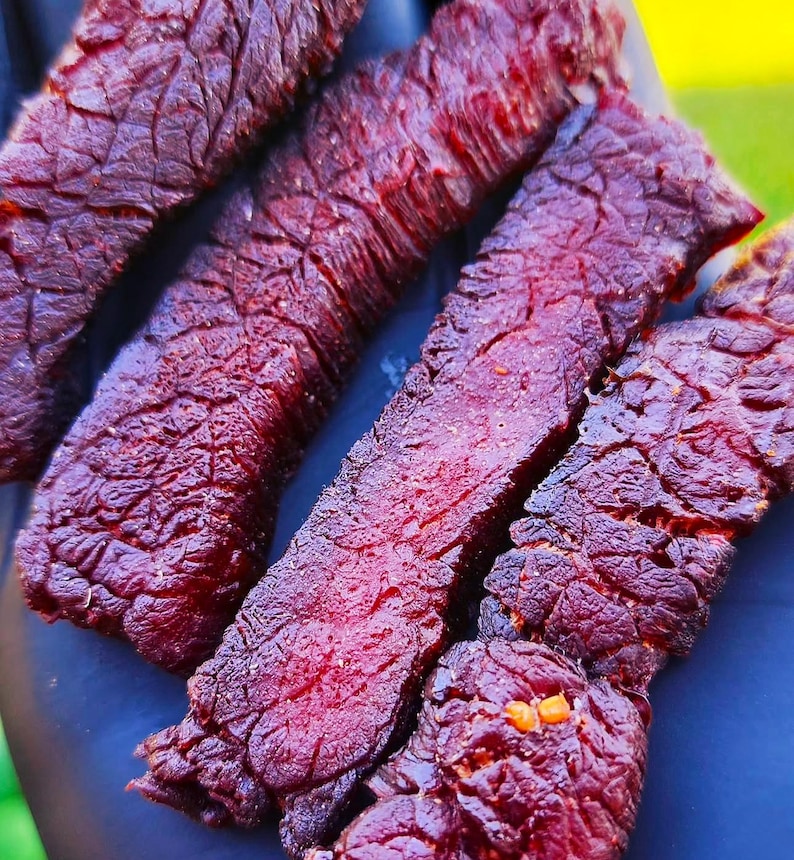 K&ouml;nnte beinhalten: Nahaufnahme von mehreren St&uuml;cken dunkelrotem Rindfleisch-Trockenfleisch. Das Trockenfleisch ist zu einem Stapel angeordnet und zeigt die Textur und Farbe des Fleisches.