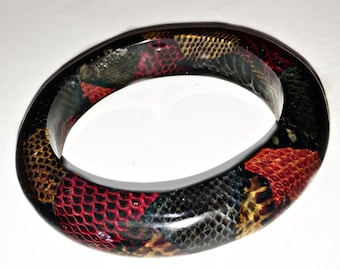 May include: A black bangle bracelet with a colorful snakeskin pattern. The pattern includes red, yellow, and black.