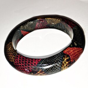 May include: A black bangle bracelet with a colorful snakeskin pattern. The pattern includes red, yellow, and black.