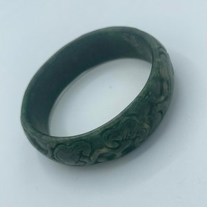 May include: A green jade bangle with intricate carved floral designs.