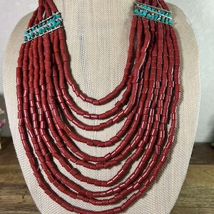 May include: A multi-strand necklace made of red coral beads with turquoise and silver accents. The necklace is layered and has a cascading effect.