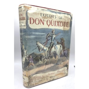 Könnte beinhalten: Ein Vintage-Hardcover-Buch mit dem Titel "Exploits of Don Quixote" mit einer Illustration eines Ritters zu Pferd. Das Cover hat ein verblasstes blau-weißes Farbschema mit dem Titel in fetten, roten Buchstaben. Das Buch ist "Retold by James Reeves."