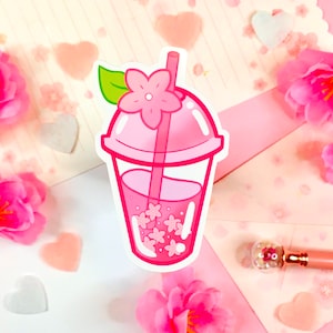 May include: A pink and white cartoon illustration of a boba tea drink with a pink flower and green leaf on top. The drink is in a clear cup with a pink lid and a straw.