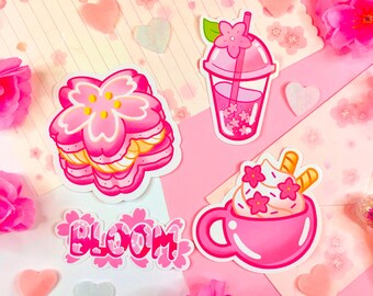 May include: Four pink and white stickers with a cherry blossom theme. The stickers feature a stack of cherry blossom cookies, a pink drink with a straw, a pink cup of whipped cream with a cherry blossom on top, and the word "BLOOM" in pink and white.