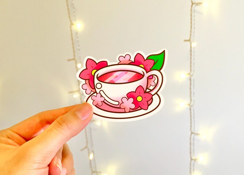 May include: A white teacup with pink flowers and a green leaf on a pink saucer. The teacup is filled with pink liquid.