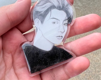 May include: A clear keychain with a black and white image of a person's face. The background of the keychain is filled with black glitter.