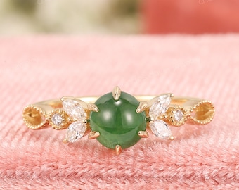 Peut inclure: Une bague en or avec une pierre précieuse verte entourée de petits diamants. La bague a un design floral délicat.
