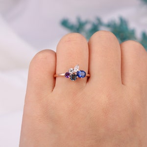 May include: A rose gold ring with a cluster of colorful gemstones. The ring features a large oval blue sapphire, a smaller round blue sapphire, a round purple amethyst, and two round white diamonds.