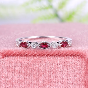 May include: A delicate silver band ring with a row of five marquise-shaped ruby gemstones and smaller round diamonds set in between each ruby.