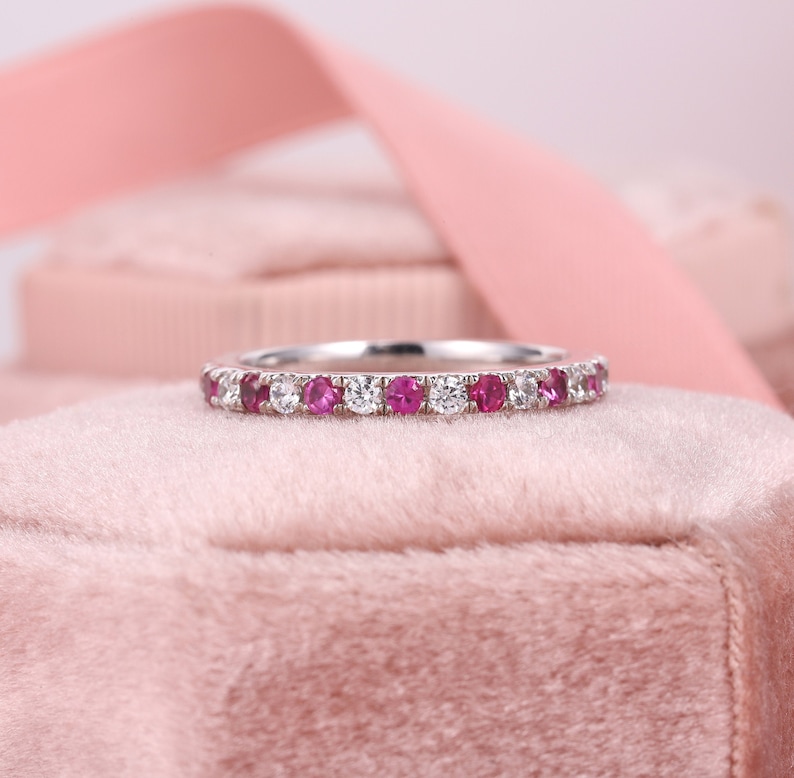 Op de afbeelding: Een delicate eeuwigheidsband met afwisselende roze saffieren en witte diamanten gezet in een gepolijste witgouden band.