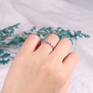 Op de afbeelding: Een delicate eeuwigheidsring met een rij kleine roze en witte edelstenen gezet in een zilveren band.