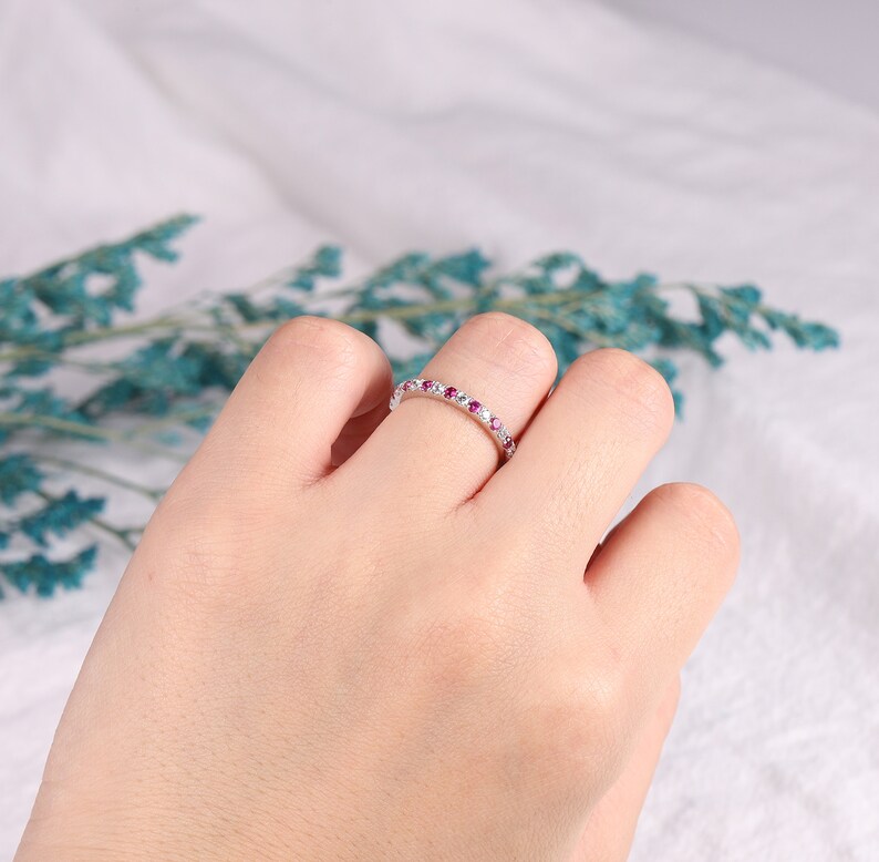 Op de afbeelding: Een delicate eeuwigheidsring met een rij kleine roze en witte edelstenen gezet in een zilveren band.