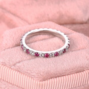 Op de afbeelding: Een delicate eeuwigheidsring met een rij kleine, ronde, rode robijnen en witte diamanten gezet in een witte metalen band.