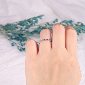 Op de afbeelding: Een delicate eeuwigheidsring met een rij kleine roze edelstenen en witte accenten.