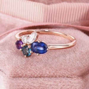May include: A rose gold ring with a cluster of gemstones. The ring features a marquise-shaped diamond, a round sapphire, a round amethyst, and a round blue topaz.