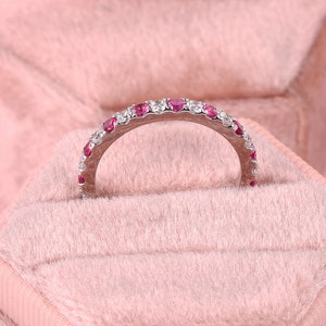 Op de afbeelding: Een delicate zilveren bandring met een rij kleine rode en witte edelstenen.