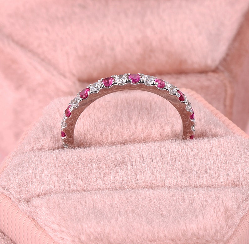 Op de afbeelding: Een delicate zilveren bandring met een rij kleine rode en witte edelstenen.