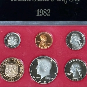 May include: A 1982 United States Proof Set in a black and red case. The set includes various coins, such as a penny, dime, and half-dollar, with detailed engravings. The case is labeled "United States Proof Set" and the year.